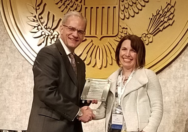 Man and woman on stage pose for photo with award