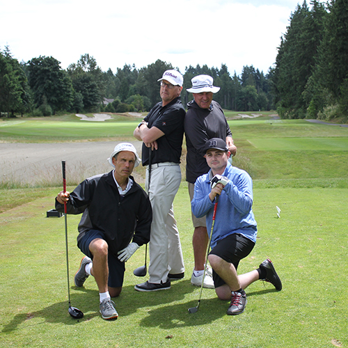 Four white men pose at a hole on a golf course